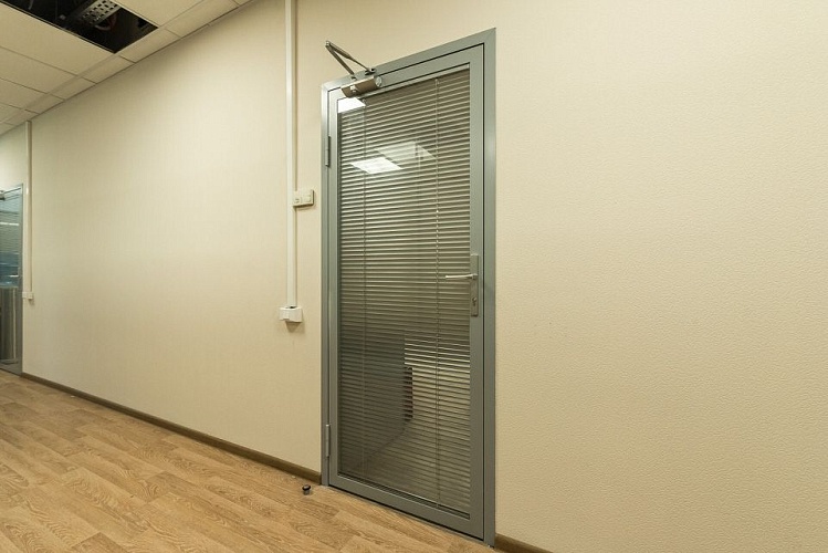 Дверь со стеклом и встроенными жалюзи, оснащенная доводчиком, в офисном коридоре