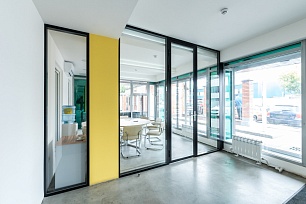 Угловая стеклянная перегородка в черном профиле в офисе у витражного окна